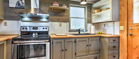 Une cuisine équipée d’une cuisinière en acier inoxydable, de meubles de rangement en bois, d’une fenêtre et d’une porte en bois.