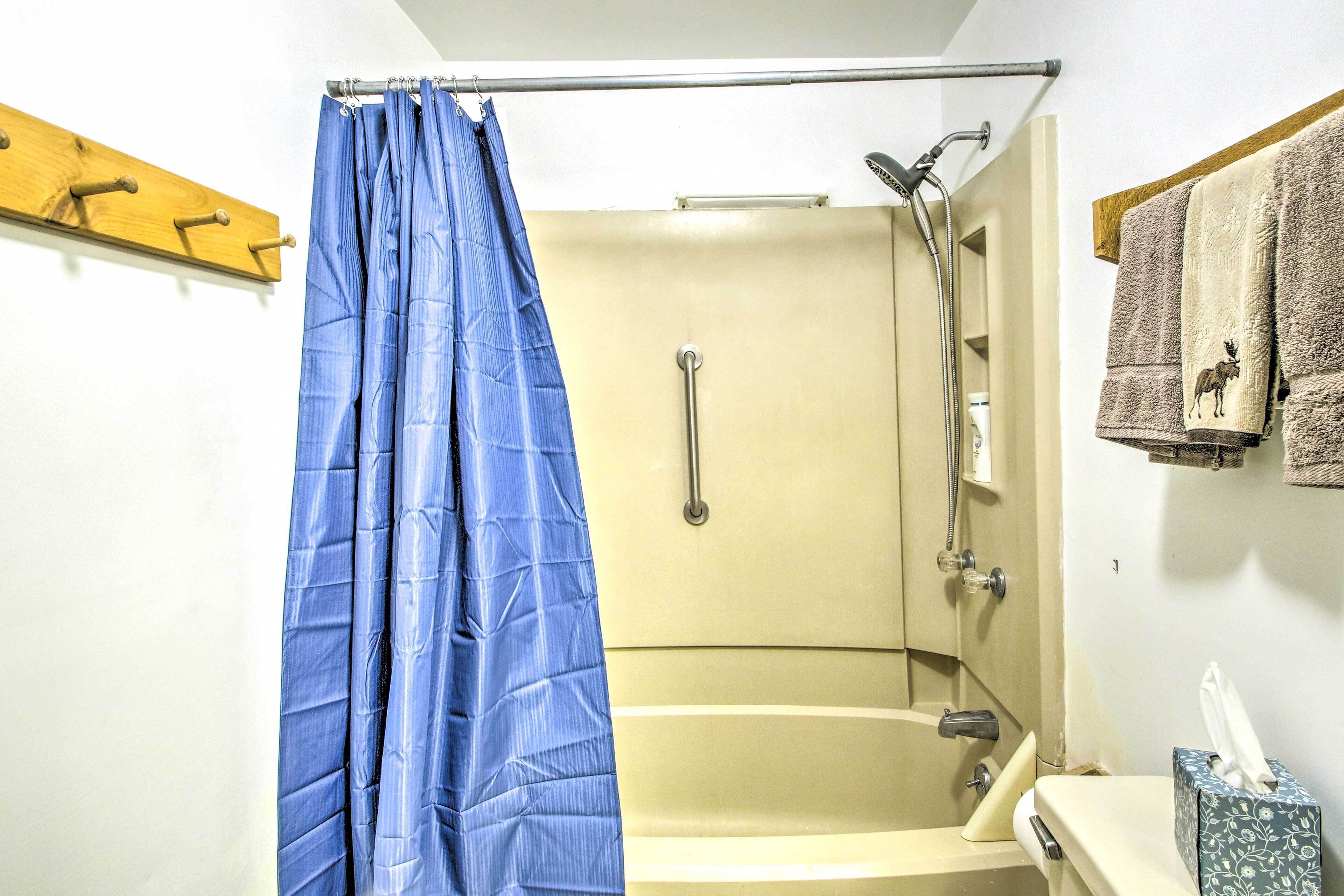 A shower with a blue curtain, a towel rack with towels, and a tissue box on the sink.