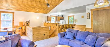 L’intérieur chaleureux d’un chalet avec un plafond en bois, un coin repas, une cuisine et un salon comprenant deux canapés et une petite table ronde.