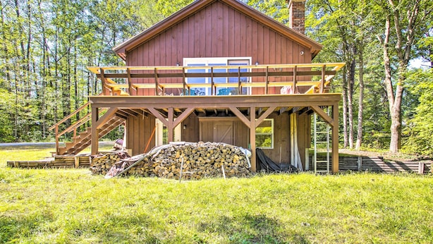 Een houten chalet met een balkon, een trap en een stapel hout ervoor.