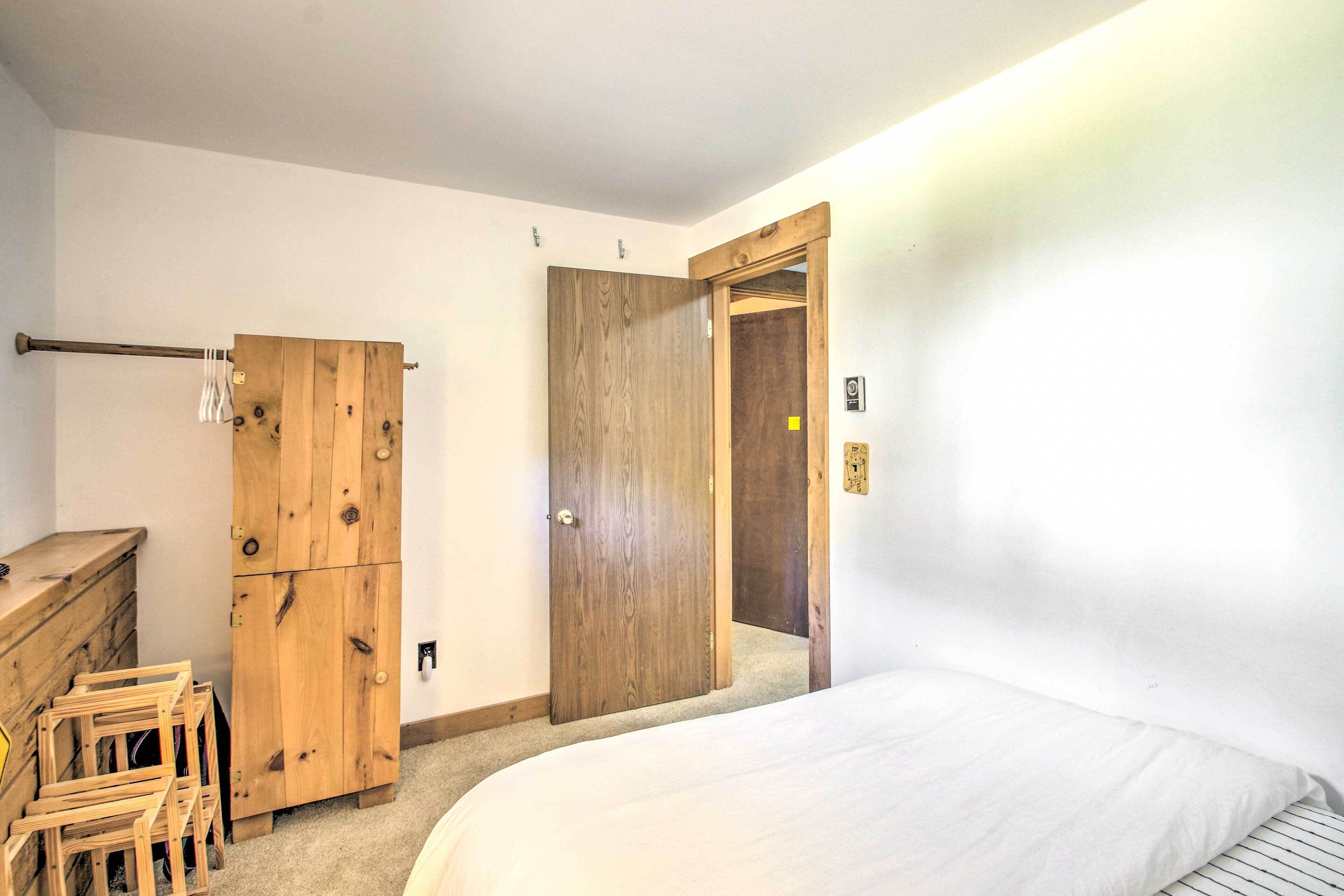 A bedroom with a wooden wardrobe, a bed, and a door leading to another room.