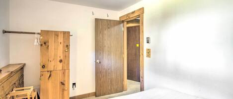 A bedroom with a wooden wardrobe, a bed, and a door leading to another room.