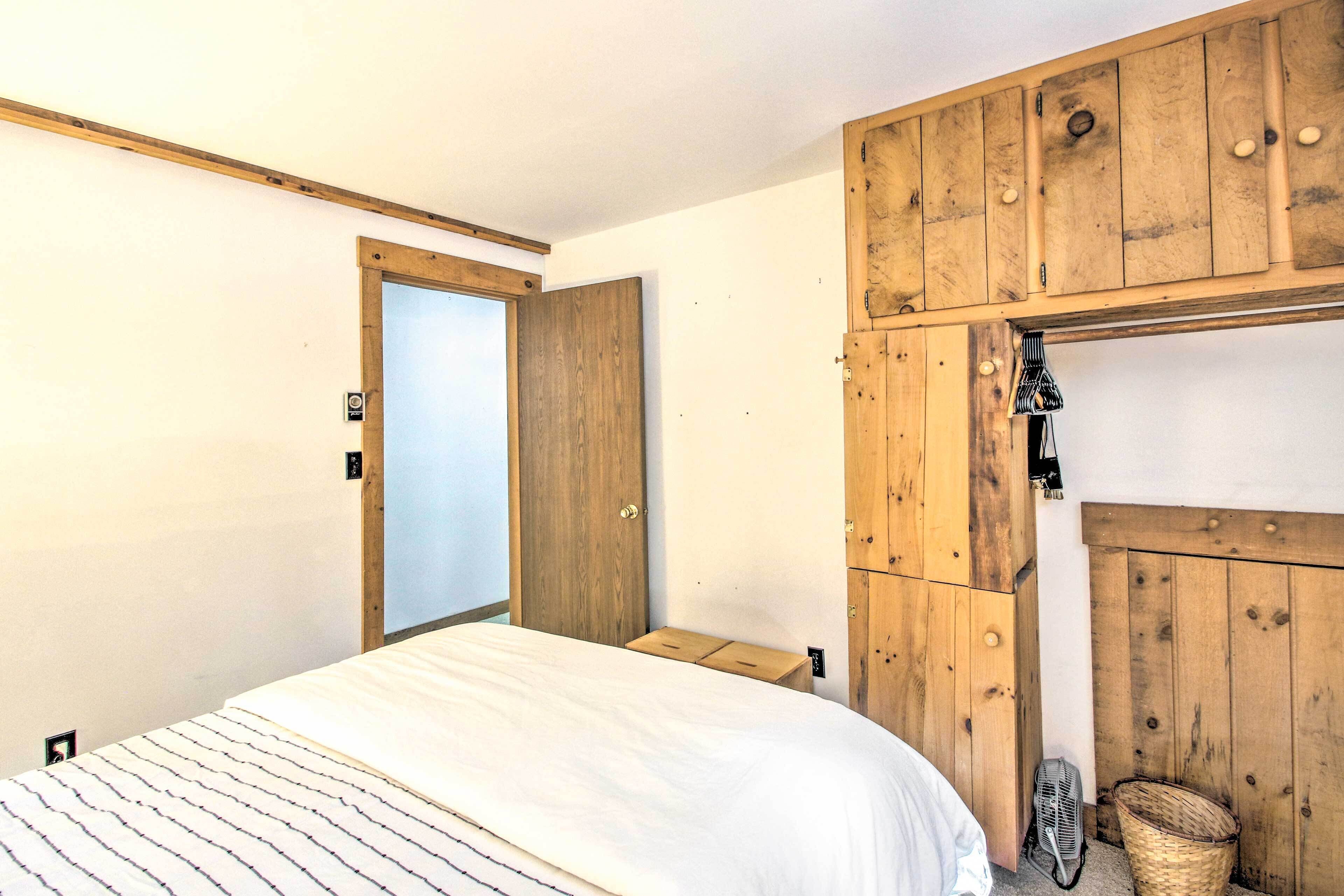 A bedroom with a wooden wardrobe, a bed with a striped bedspread, and a small bedside table.