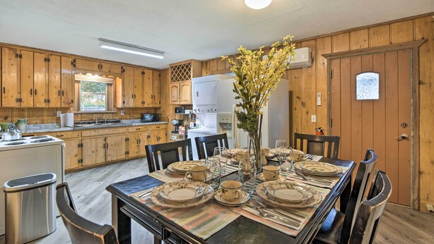 Une cuisine avec des meubles de rangement en bois, une table à manger dressée pour six personnes et un réfrigérateur.