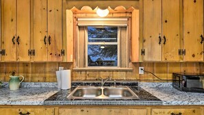 Une cuisine avec des meubles en bois, un évier à deux bacs, une fenêtre avec vue et un plan de travail sur lequel se trouvent une bouilloire et un grille-pain.
