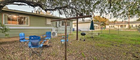 A residential backyard with a covered patio area, outdoor seating, and a barbecue grill.