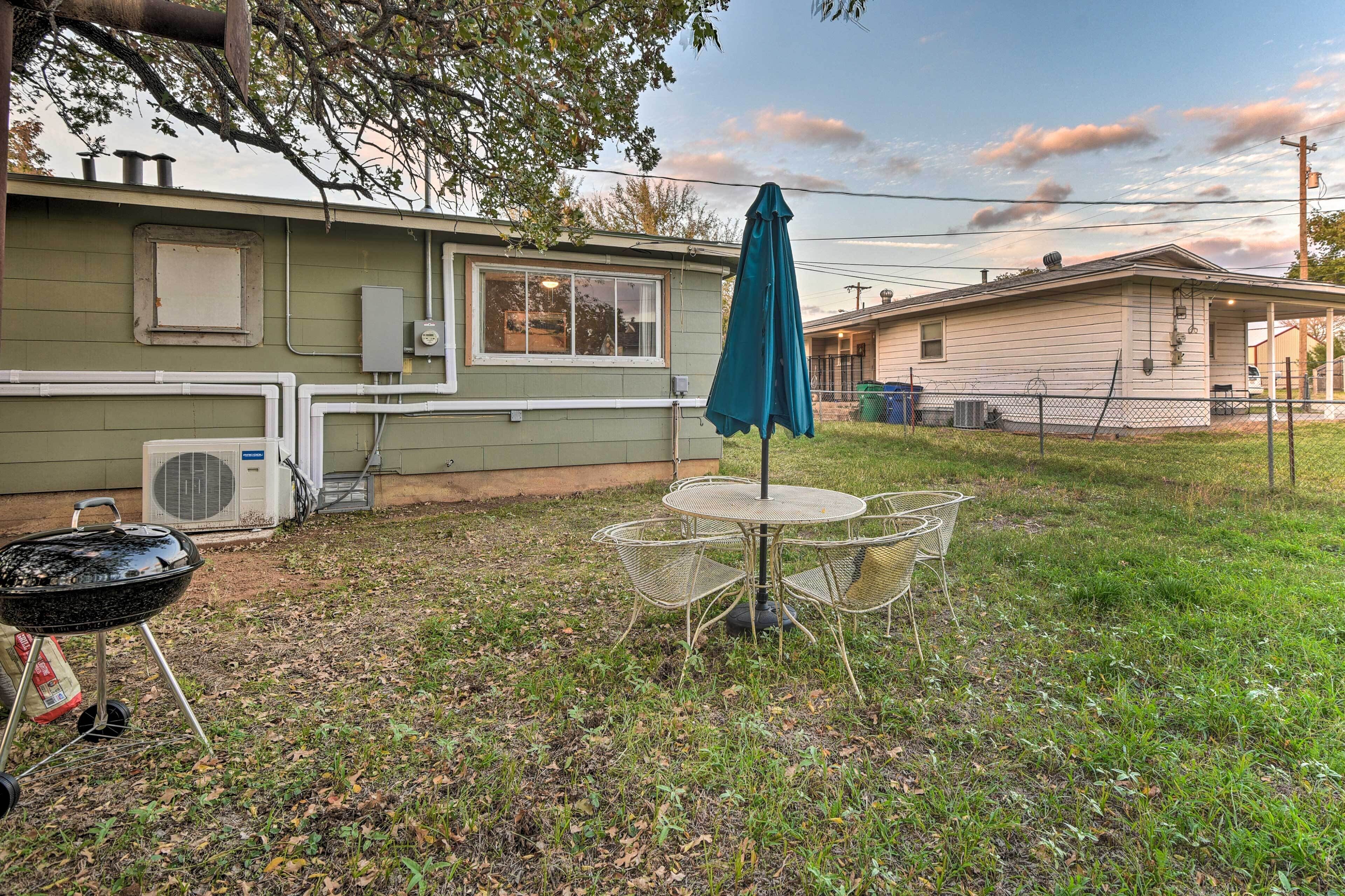 A backyard with a grill, a table with chairs, and a covered umbrella.