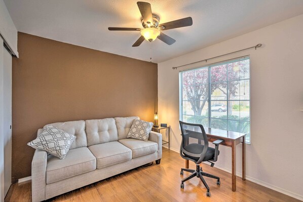 A room with a beige sofa, a wooden desk, and a ceiling fan.