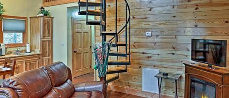 A spacious living room with a brown leather sofa, a wooden staircase, a fireplace, and a television.