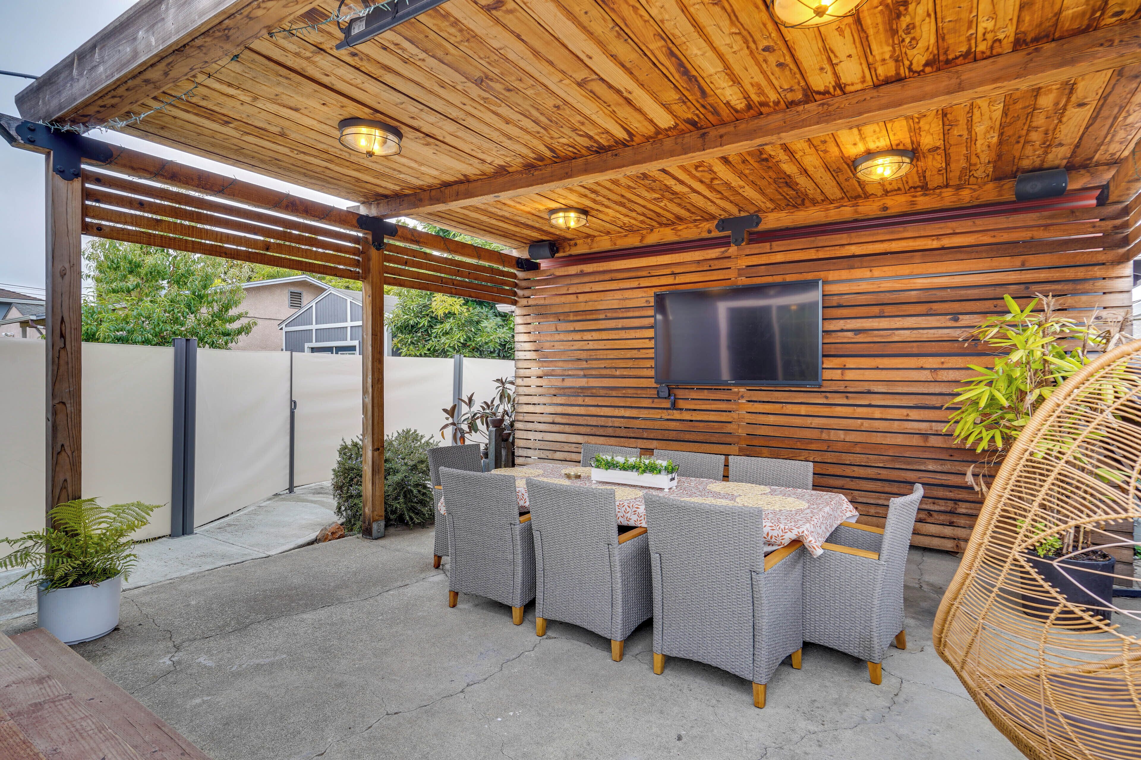 Un patio al aire libre con techo de madera, una mesa con sillas y un televisor de pantalla plana montado en la pared.