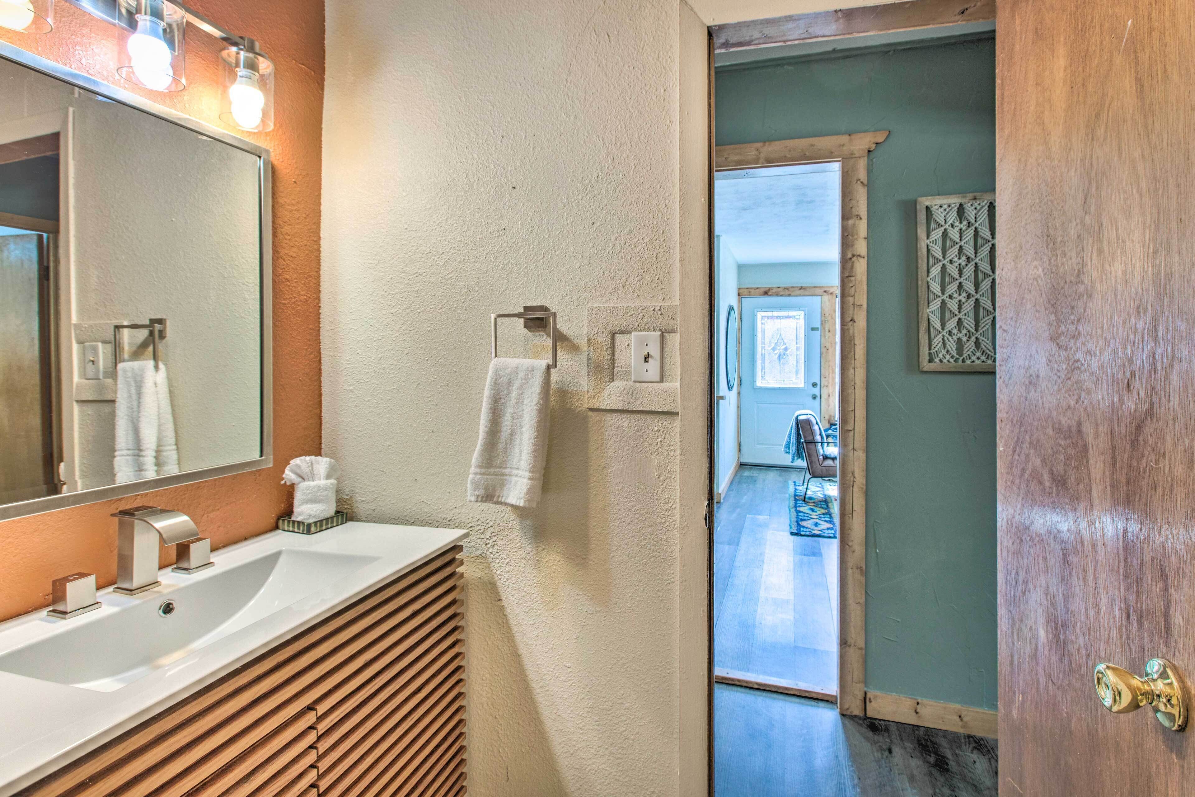 Un baño con un espejo grande, un lavamanos y un perchero para toallas.