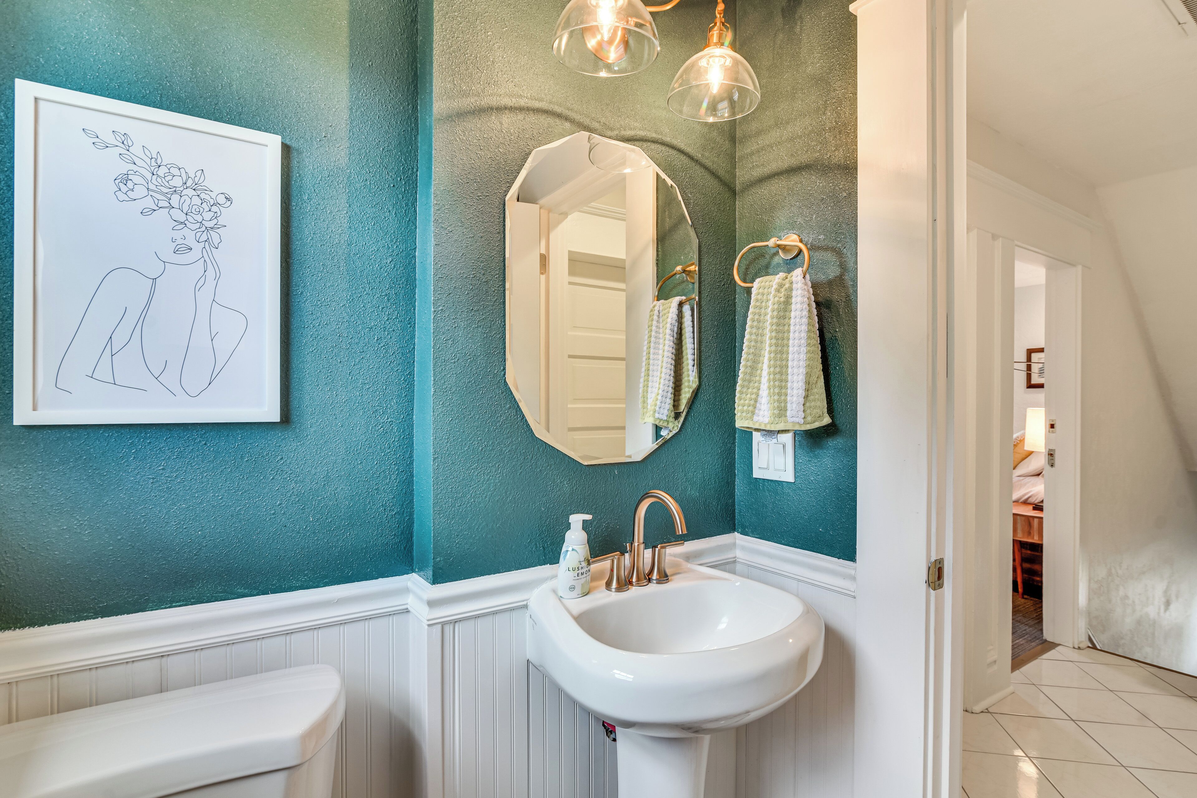 A bathroom with teal walls, a white sink, a framed line drawing, and a mirror with a towel rack.