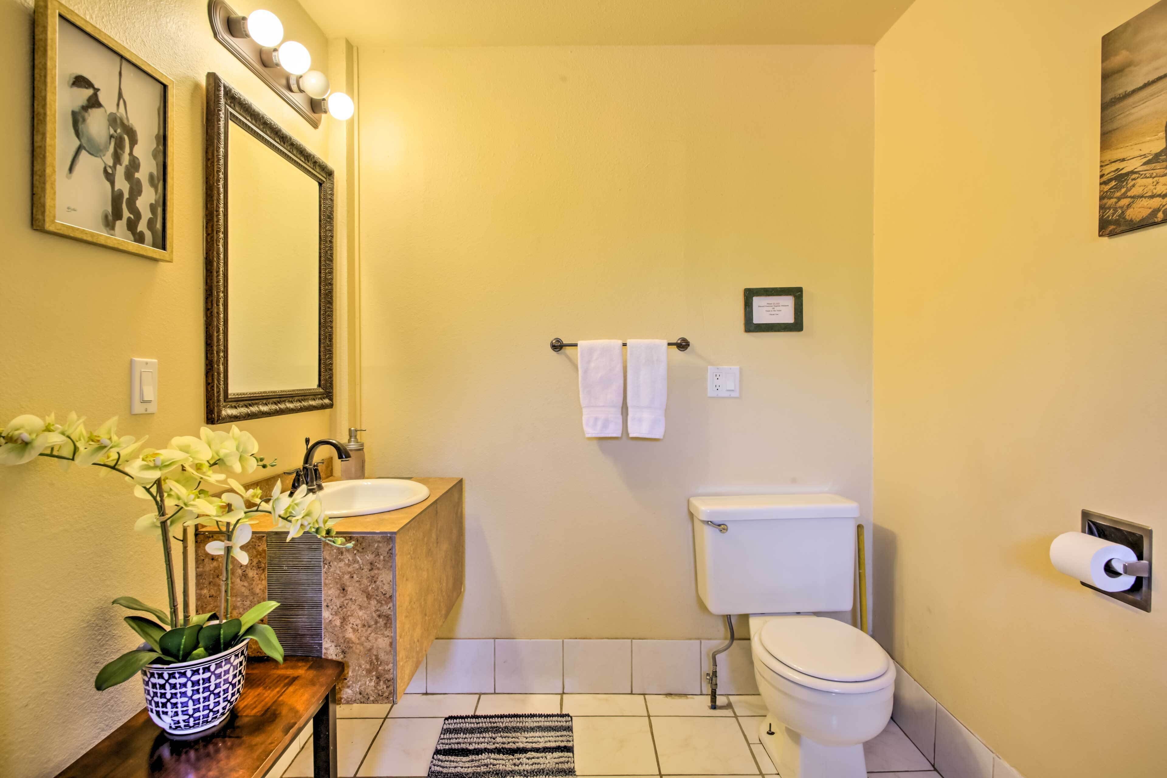 A bathroom with a sink, mirror, toilet, and a potted orchid.