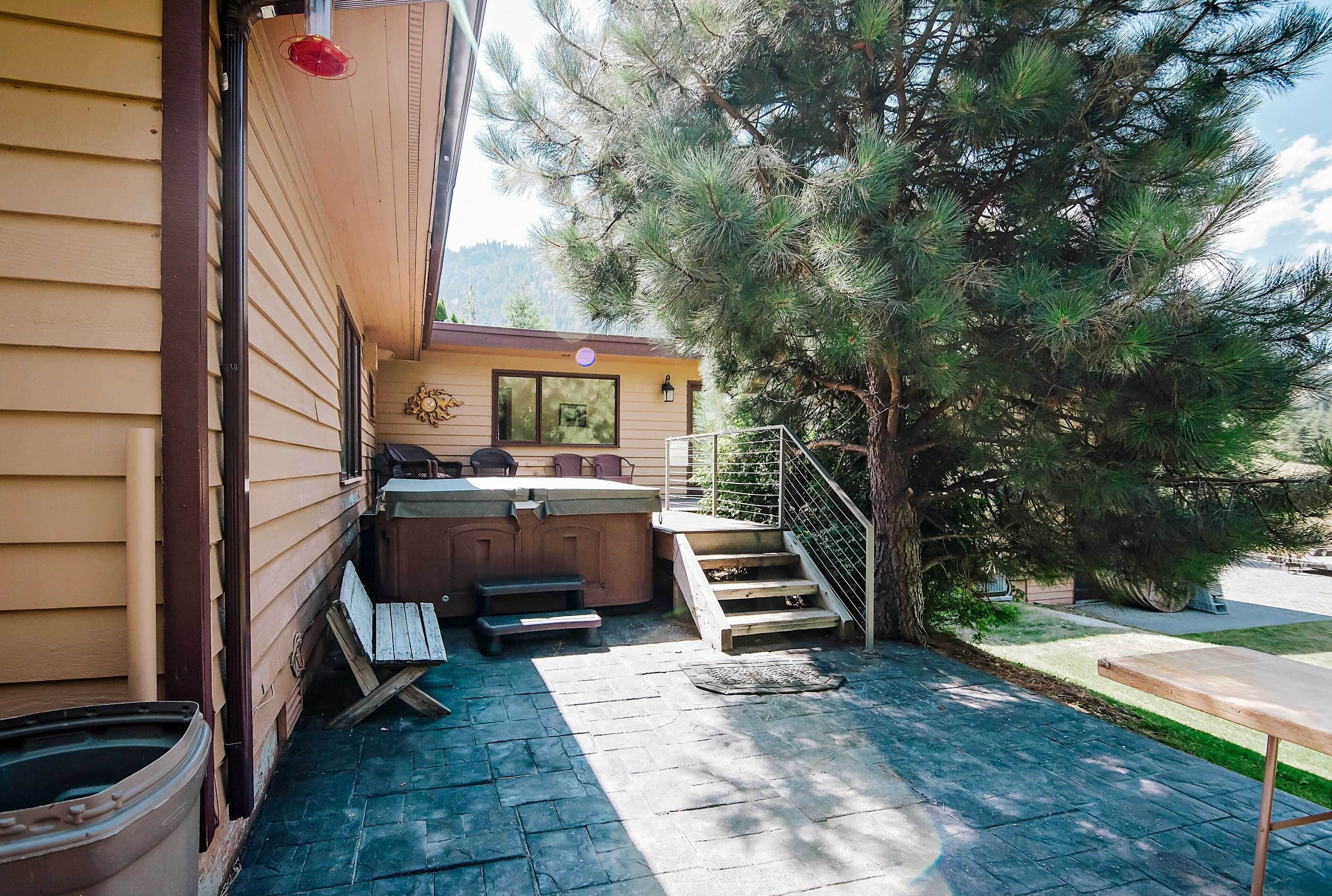 A patio area with a hot tub, steps leading to a deck, and a large tree.
