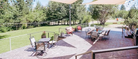 Un espace extérieur aménagé en terrasse, avec des tables et des chaises, un vélo, et une vue sur un champ verdoyant et des arbres.