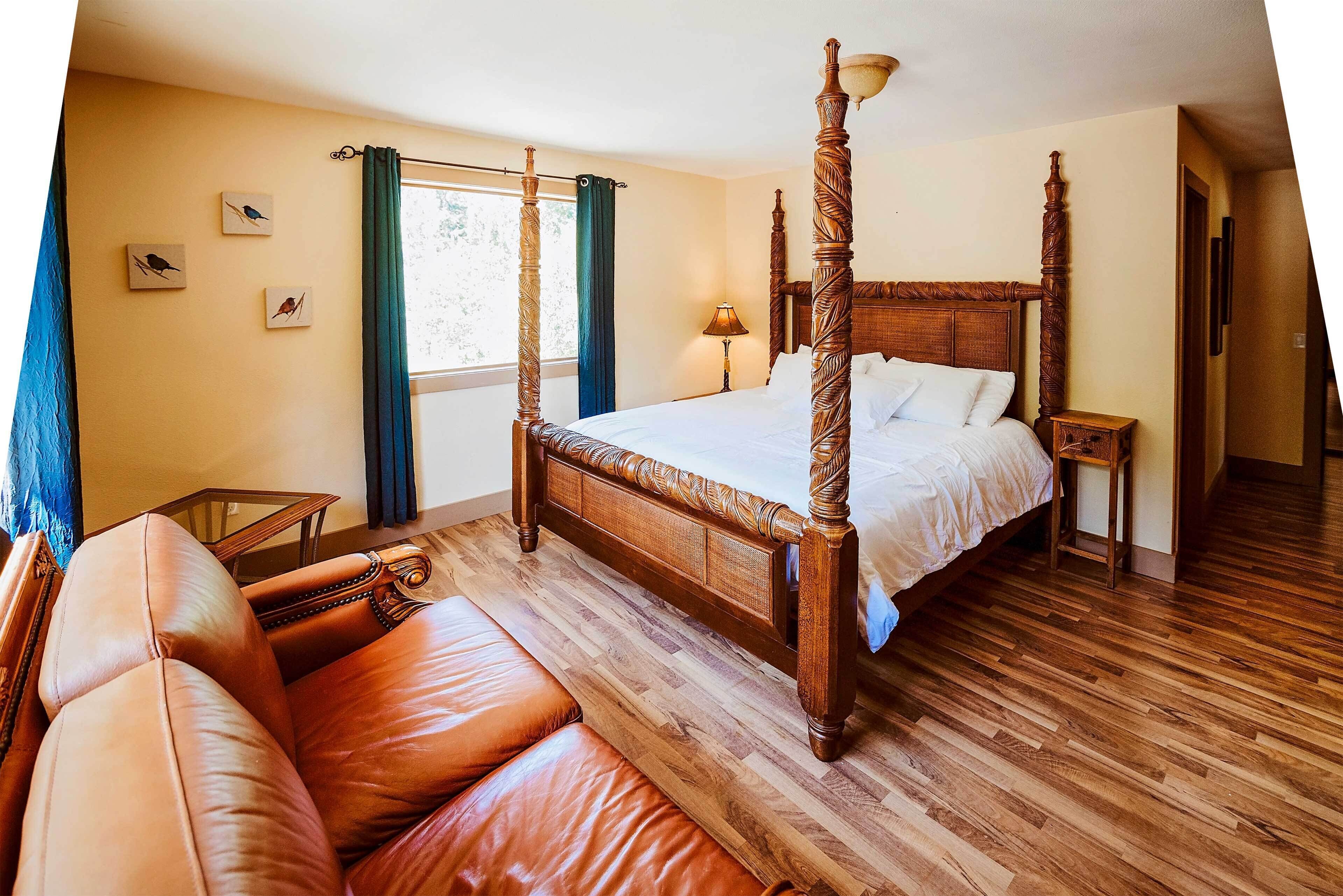Una cama con dosel y tablero de madera, un sofá de cuero y una mesita de noche de madera con una lámpara.