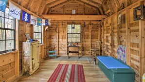 Een rustiek houten blokhutinterieur met een hoogslaper, een kleine tafel en een raam met uitzicht op het bos.