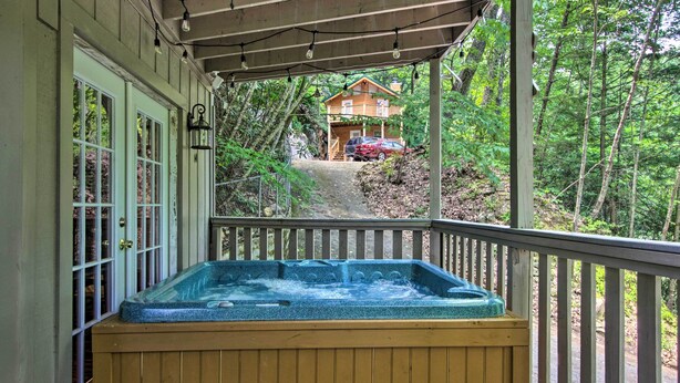 A wooden deck with a hot tub, a covered porch, and a view of a cabin in a forested area. - Rustic Gatlinburg Chalet w/ Hot Tub: 2 Mi to Town (Gatlinburg)