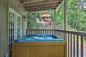 Une terrasse en bois avec un jacuzzi, une véranda et une vue sur un chalet situé dans une zone boisée.