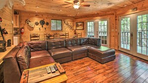 A log cabin interior with a large leather sectional sofa, wooden floors, and a ceiling fan. - Rustic Gatlinburg Chalet w/ Hot Tub: 2 Mi to Town (Gatlinburg)