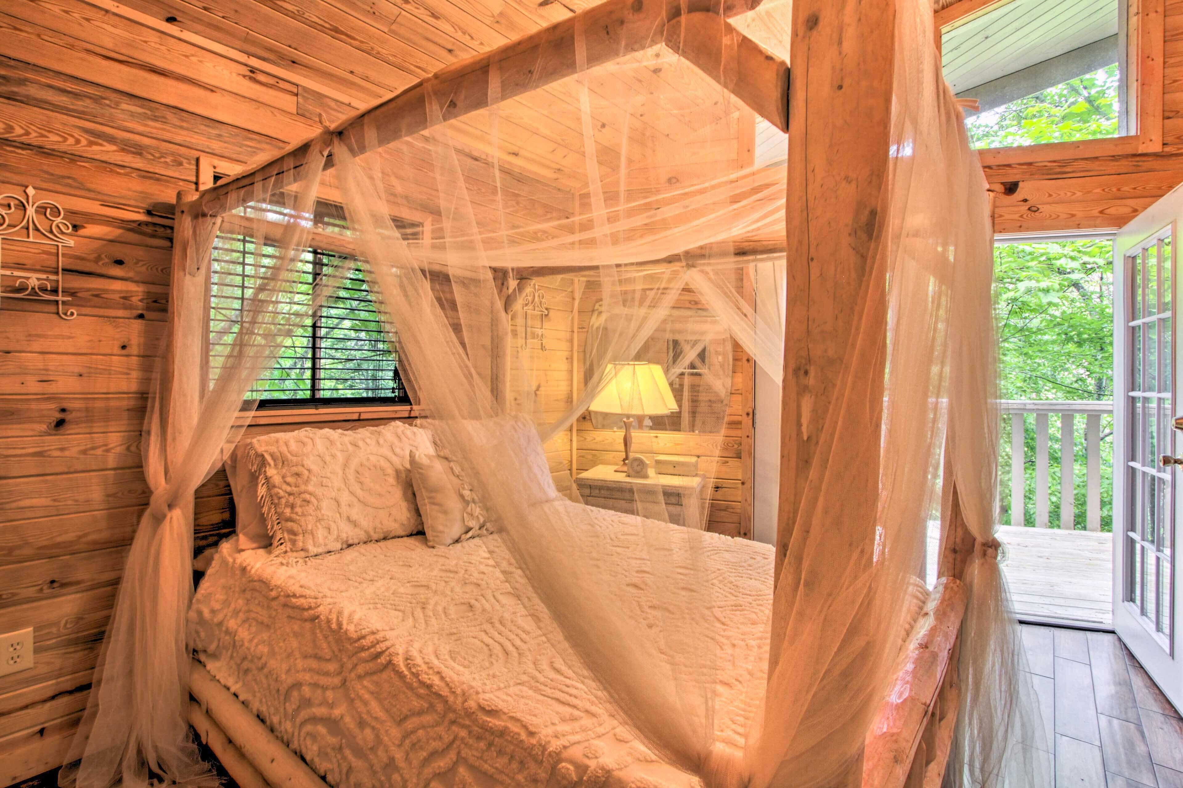 A wooden cabin bedroom with a canopy bed, a nightstand with a lamp, and a view of the outdoors.