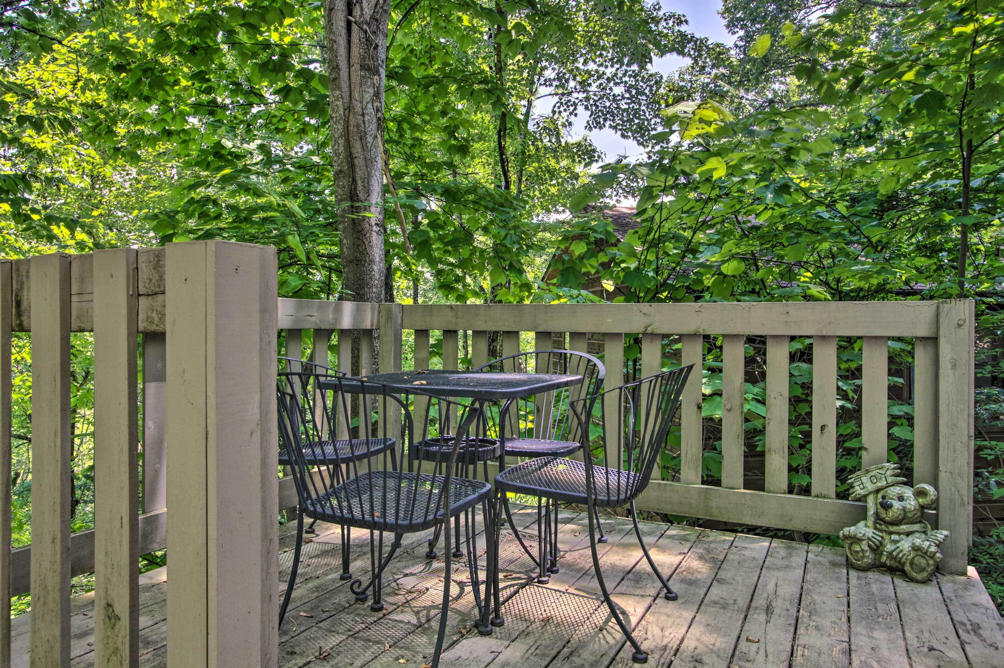 A wooden deck with a table and chairs, surrounded by lush greenery.