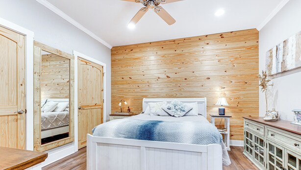 A bedroom with a wooden panel wall, a bed with a blue and white patterned bedspread, a nightstand with a lamp, and a dresser with drawers.