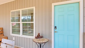 A porch with a wooden bench, a small round table with a decorative item, and a turquoise door.
