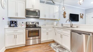 A modern kitchen with white cabinets, stainless steel appliances, and a wooden floor.