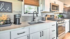 Uma cozinha moderna com armários brancos, uma pia de aço inoxidável, cafeteira e forno embutido.