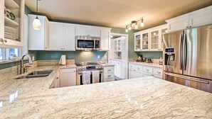 A modern kitchen with white cabinetry, a stainless steel refrigerator, a built-in oven, and a granite countertop.