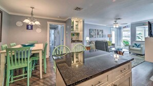 A spacious living area with a dining table, chairs, and a kitchen island. There are ceiling fans, a sofa, and a TV. - Pool w/ Spa! Beachfront Condo in Port Aransas (Port Aransas)