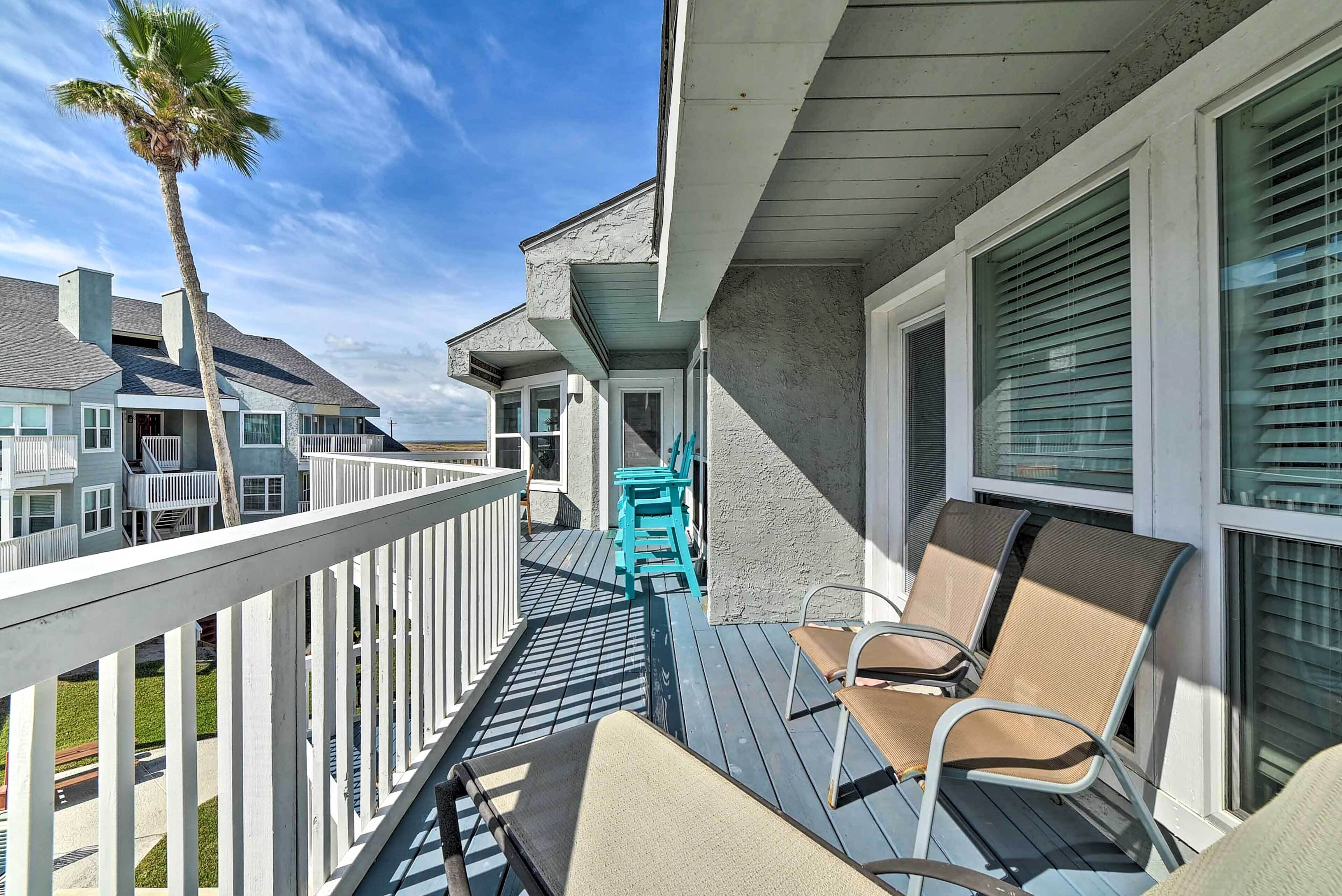 A wooden deck with outdoor furniture, a palm tree, and a view of neighboring houses.