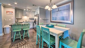 A kitchen with white cabinets, a dining area with a table and chairs, and a large window with a view of the sea. - Pool w/ Spa! Beachfront Condo in Port Aransas (Port Aransas)