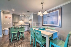 A modern kitchen with white cabinets, a dining area with teal chairs, and a large window with a view of the sea.