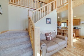 A wooden staircase leading to a loft bedroom with a beige leather sofa and a small kitchen area in the background.