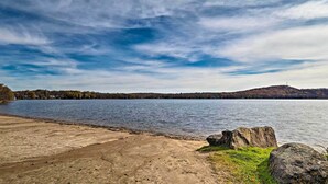 A lakeside view with a concrete walkway, large rocks, and a distant hill.
