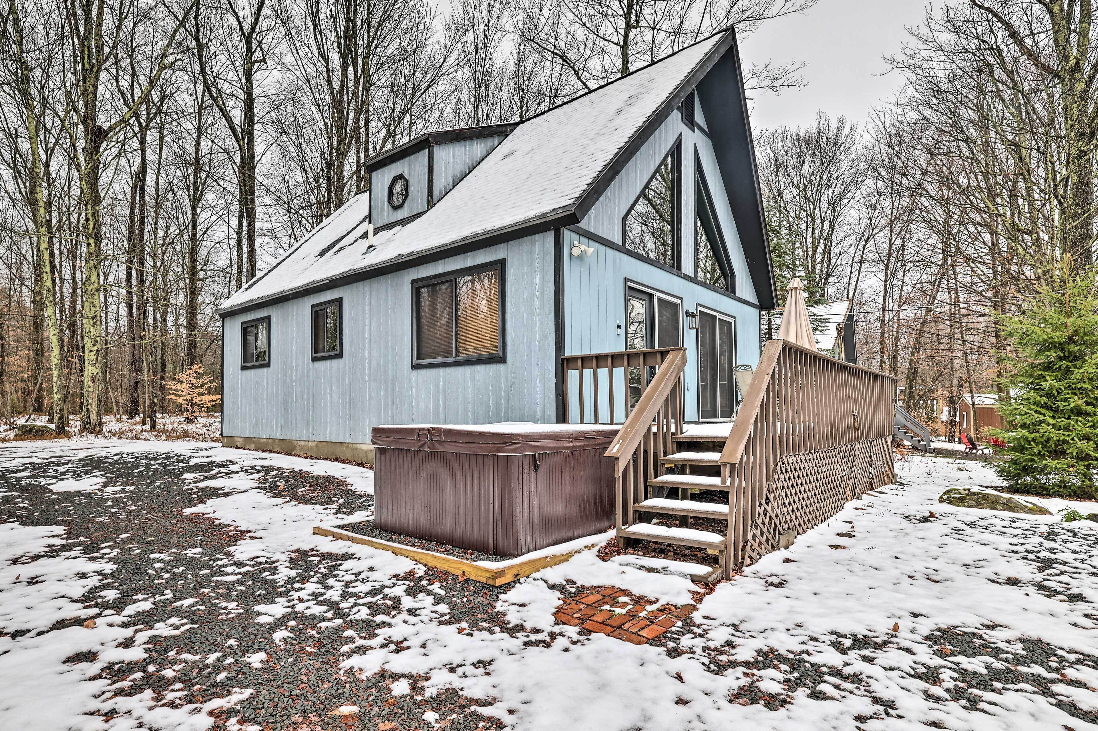 A blue cabin with a wooden staircase and a hot tub in front.