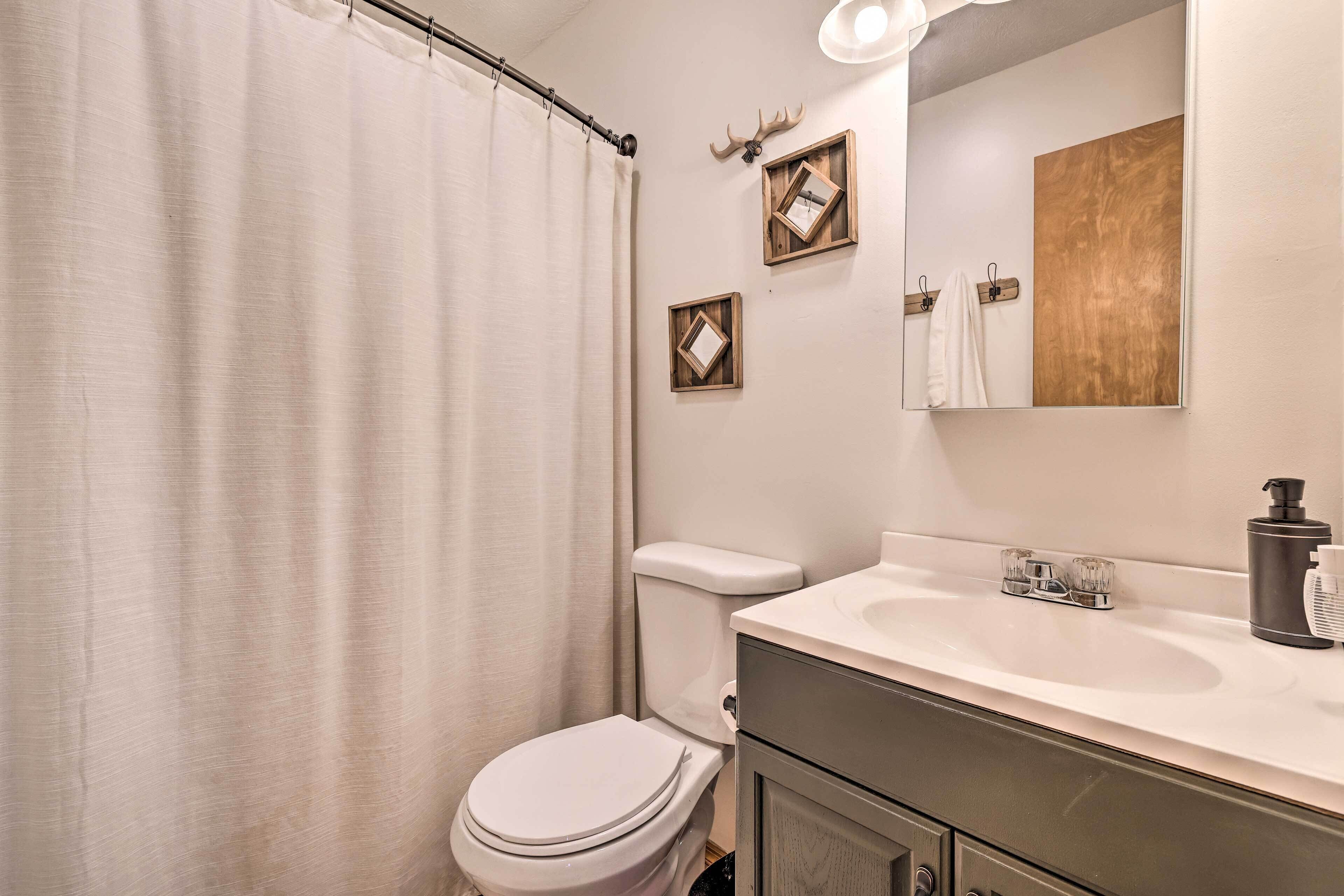 Une salle de bain avec des toilettes blanches, un lavabo avec un miroir au-dessus et un rideau de douche.