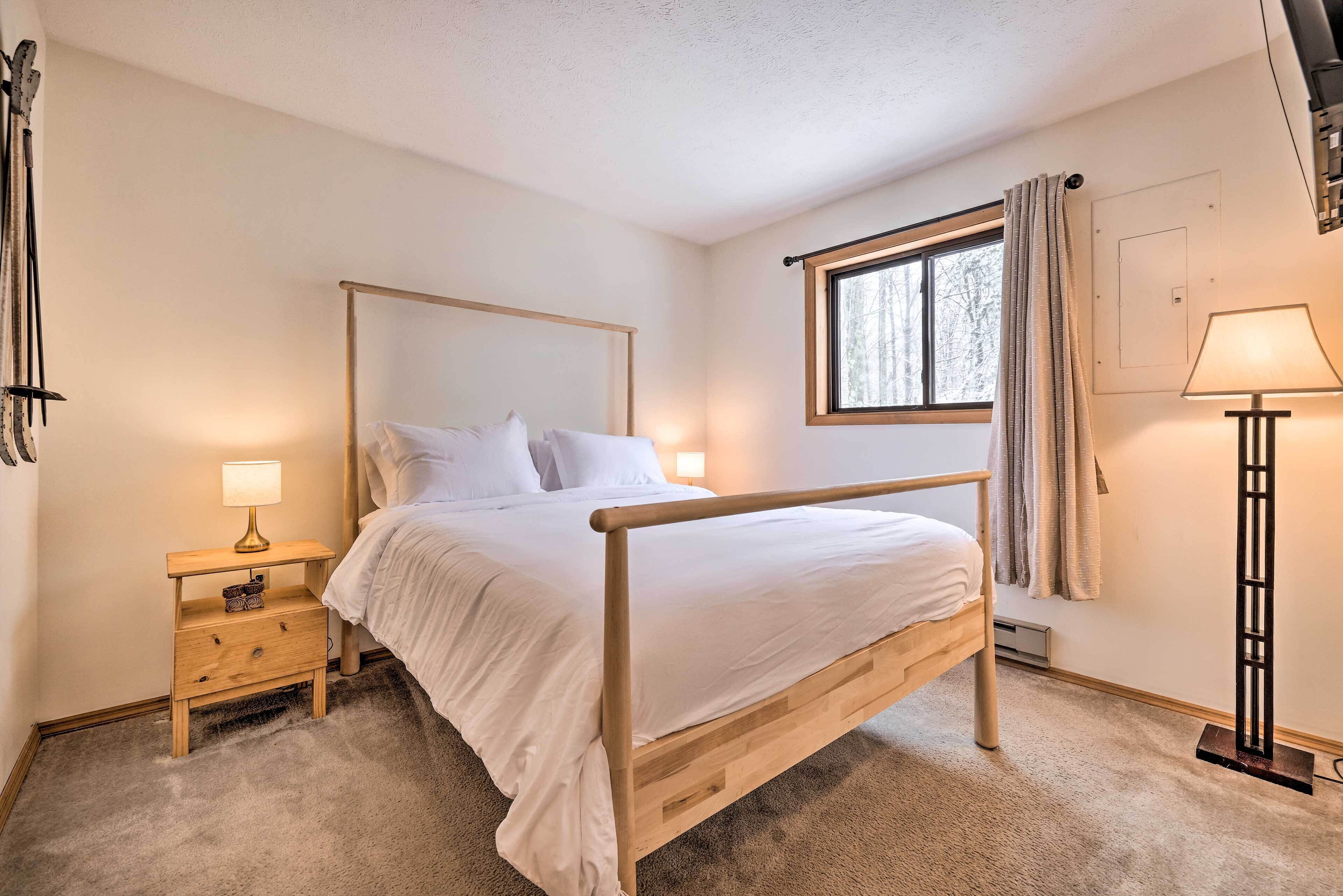 A single bed with a wooden frame, a nightstand with a lamp, and a window with curtains.