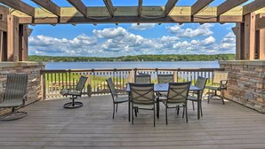 A wooden deck with a table and chairs, overlooking a body of water and green landscape.