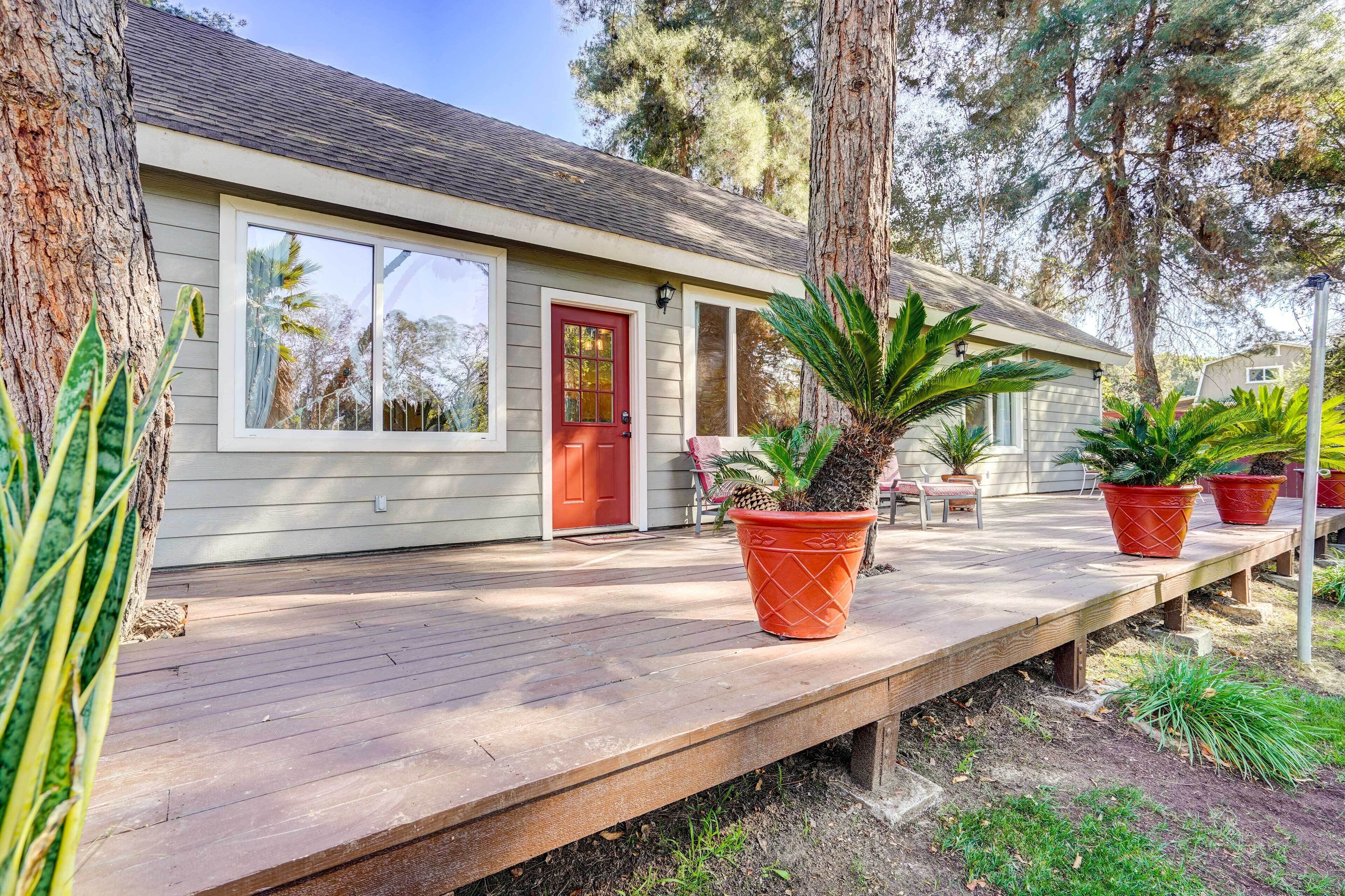 A house with a wooden deck, a red door, and potted plants.