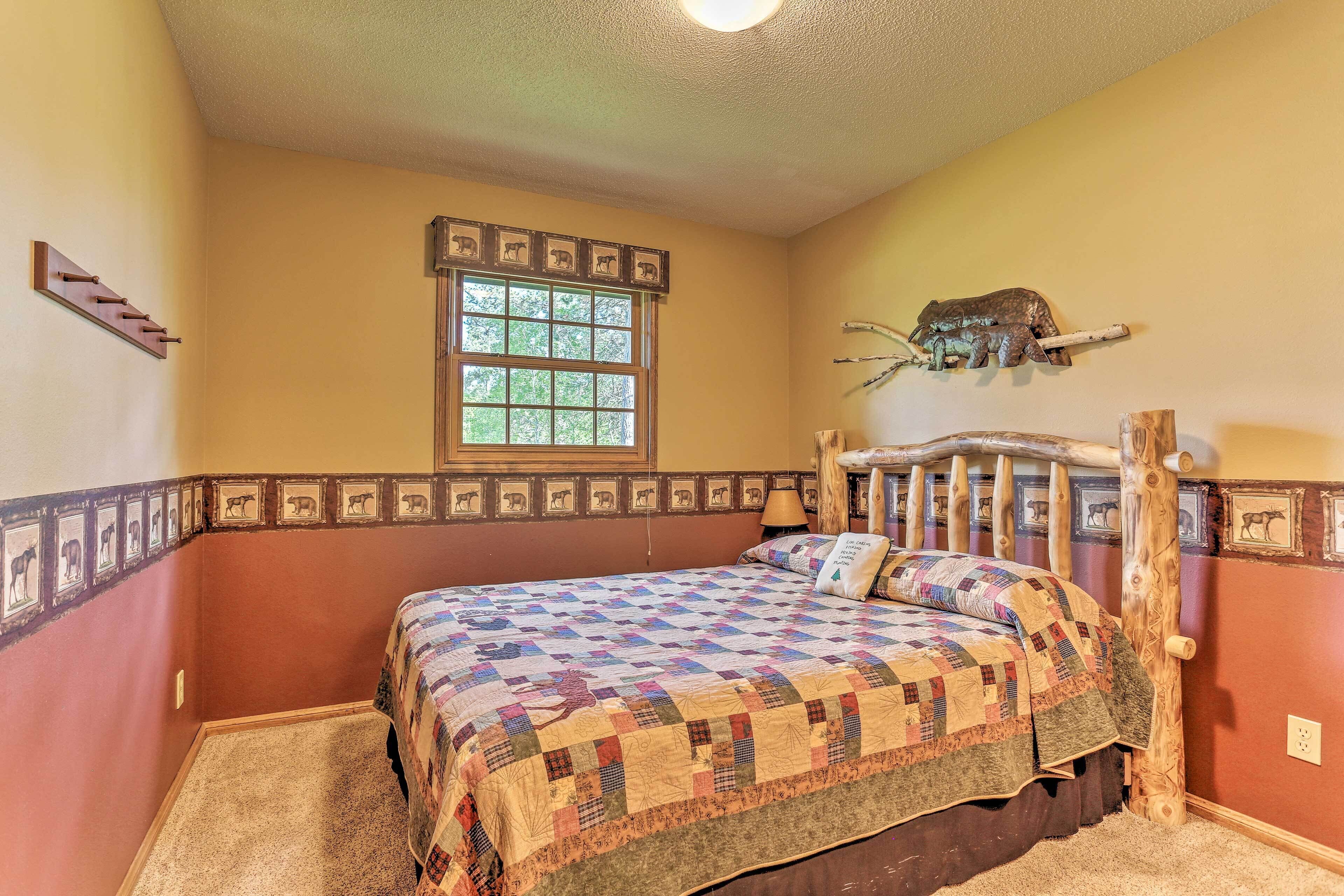 Un dormitorio con cabecera de madera, colcha acolchada, ventana con vistas a follaje y estante de pared con objetos decorativos.