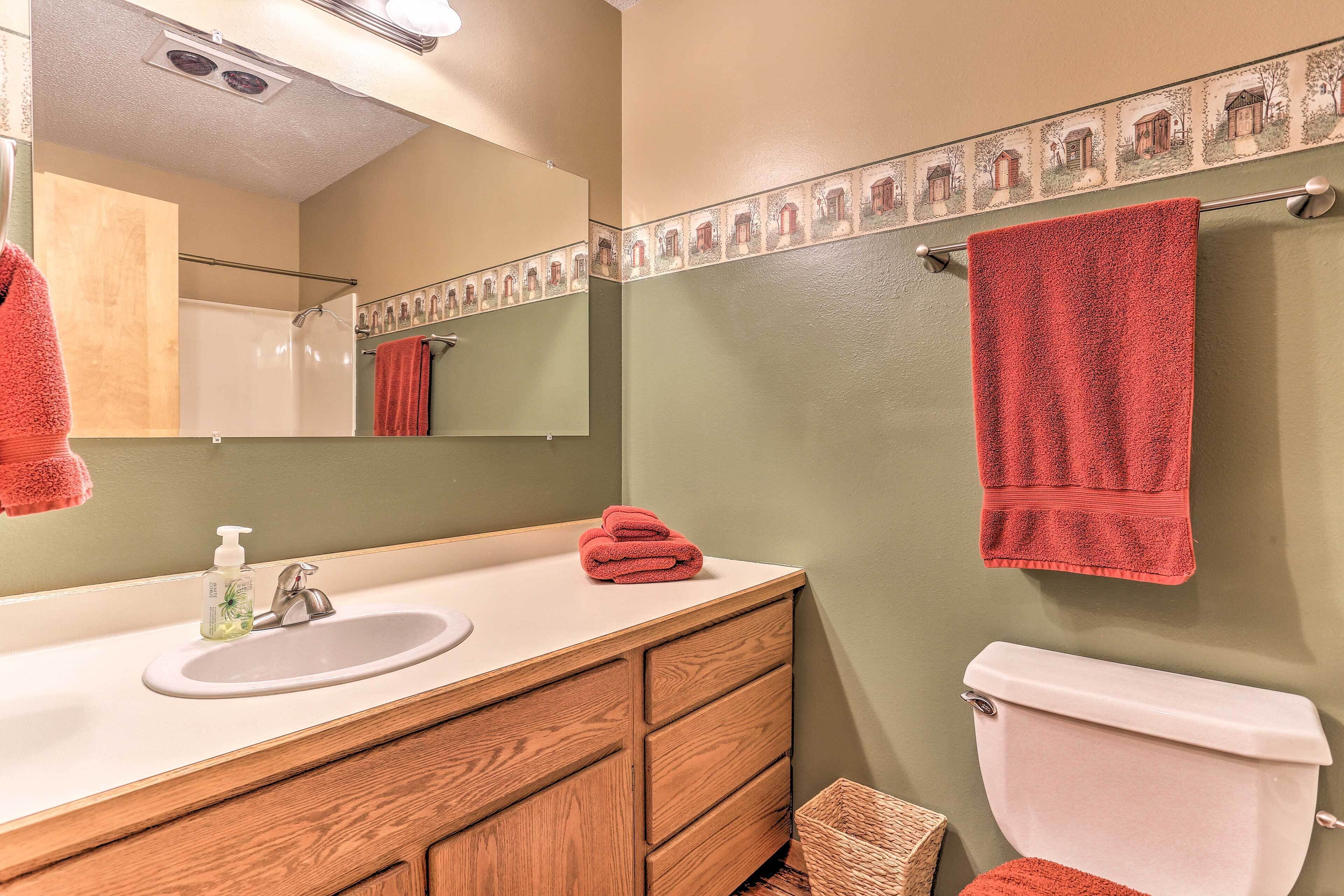 A bathroom with a wooden vanity, a white sink, a mirror, a red towel, and a toilet.