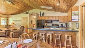A spacious kitchen with wooden cabinets, a central island with stools, a refrigerator, and a microwave. - Lead Cabin ~ 9 Mi to Deadwood: Hot Tub + Patio! (Lead)