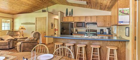 A spacious kitchen with wooden cabinets, a central island with stools, a refrigerator, and a microwave.