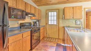 A kitchen with wooden cabinets, a stainless steel sink, a stove, and a microwave. - Lead Cabin ~ 9 Mi to Deadwood: Hot Tub + Patio! (Lead)