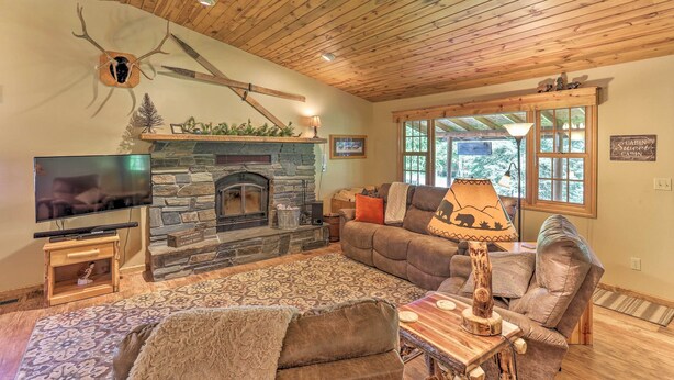 A cozy living room with a stone fireplace, a television, and comfortable seating. - Lead Cabin ~ 9 Mi to Deadwood: Hot Tub + Patio! (Lead)