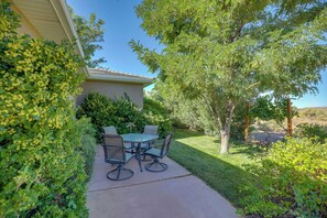 A patio with a round table and chairs, surrounded by lush greenery and a house in the background.