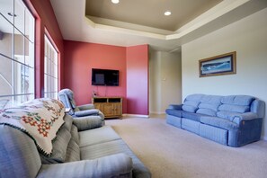 A living room with a grey sofa, a blue sofa, a wooden cabinet, and a flat-screen TV mounted on the wall.